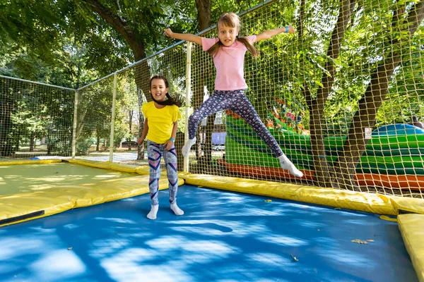 Duas meninas no salto de verão em um trampolim, sorrindo e rindo. As crianças brincam. Relaxe ao ar livre. Os amigos saltam num trampolim. Criança feliz — Fotografia de Stock