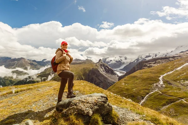 Молодая счастливая женщина с рюкзаком, стоящая на скале и глядя на долину внизу — стоковое фото