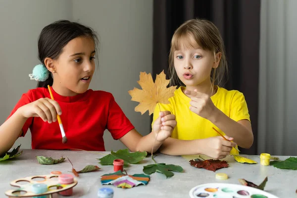 Δύο κορίτσια ζωγραφίζουν φθινοπωρινά φύλλα στο τραπέζι. — Φωτογραφία Αρχείου
