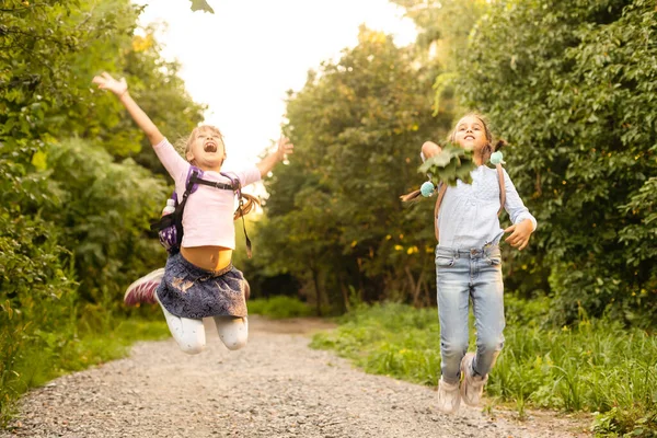 Deux filles s'amusent dans le parc, tenue d'automne. Amusants filles drôles jetant des feuilles dans la ville en automne. Bonne famille en promenade d'automne. Géasture paix. — Photo