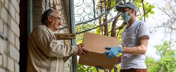 Uma idosa usando um andador recebe refeições de um homem que trabalha com um grupo benevolente entregando alimentos para aqueles que estão em alto risco por causa do coronavírus COVID19. — Fotografia de Stock