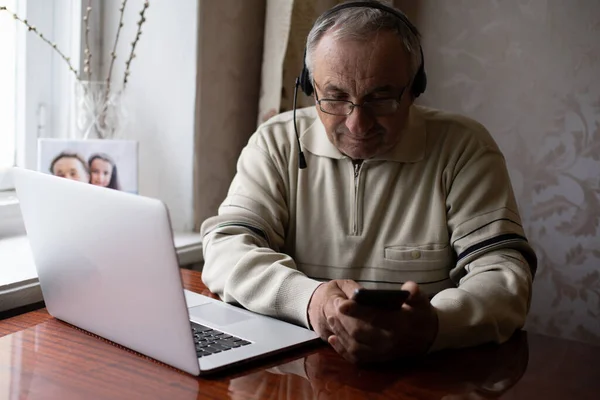 Hombre mayor usando portátil y auriculares en línea. — Foto de Stock