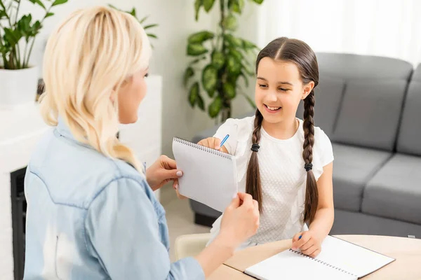 Mãe e filha bonita e feliz fazer um cartão para o dia das mães sentadas juntas à mesa com papel e lápis — Fotografia de Stock