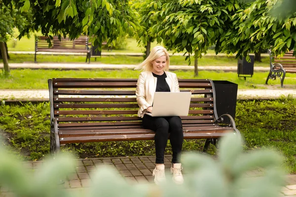 Молодая привлекательная деловая женщина, сидя на деревянной скамейке в городском парке, за компьютером с ноутбуком. — стоковое фото