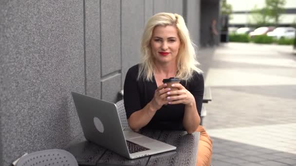 Молодая женщина носит умные часы, используя ноутбук. Женщина работает на ноутбуке в кафе под открытым небом . — стоковое видео
