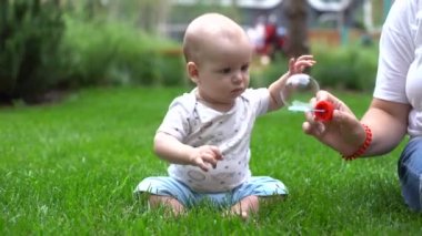 sabun köpüğü ile oynarken açık yeşil çimenlerin üzerinde oturan erkek bebek