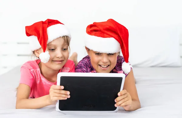 Heyecanlı küçük kardeş çocuklar modern tablet aletleriyle oynarken eğleniyorlar. Mutlu küçük kız çocukları ped cihazıyla video izleyip, kış tatillerinde evde eğleniyorlar.. — Stok fotoğraf