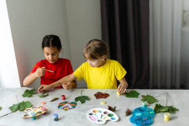 Masada sonbahar yapraklarını boyayan iki kız..