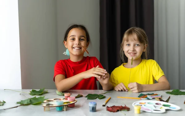 Duas meninas pintam folhas de outono à mesa. — Fotografia de Stock