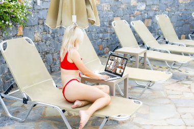 güneşlenme havuzu tarafından üzerinde rahatlatıcı iken dizüstü bilgisayar kullanan kadın