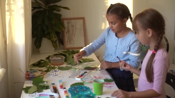 Дві школярки малюють листя, дівчата малюють осіннє листя — стокове відео