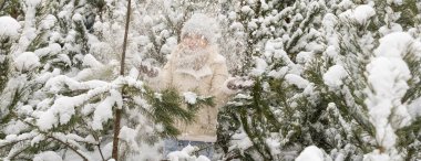 Beyaz elbiseli bir kız karda bir çam ağacının yanında duruyor..