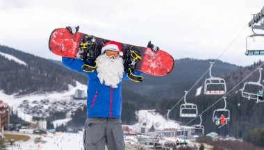 Kar kayağına karşı kar kayağı yapan Noel Baba. Kayak merkezi manzarası ve mavi gökyüzü. Yeni yıl veya xmas tebrik kartı..