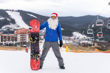 Kış Dağları tepesinde kar kayağıyla Noel Baba şapkalı mutlu bir adam.