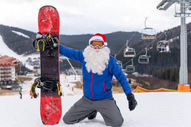 Kayak merkezinde kar kayağı yapan Noel Baba şapkalı bir adam.