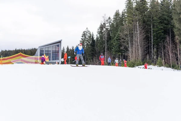 Santa Claus se snowboardem proti zasněžené zimní horské lyžařské středisko krajina a modrá obloha, Nový rok nebo vánoční přání. — Stock fotografie