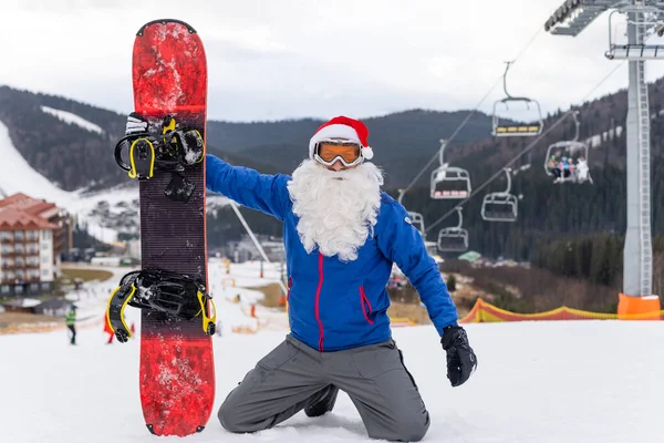 Um homem de chapéu de Pai Natal com um snowboard em uma estação de esqui — Fotografia de Stock