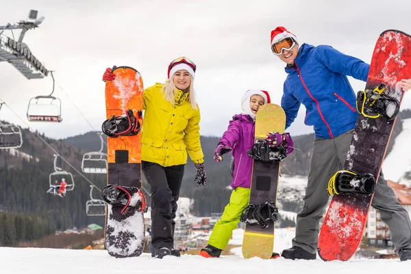 Портрет счастливой семьи в кепках Санта-Клауса и сноуборде на зимнем курорте — стоковое фото