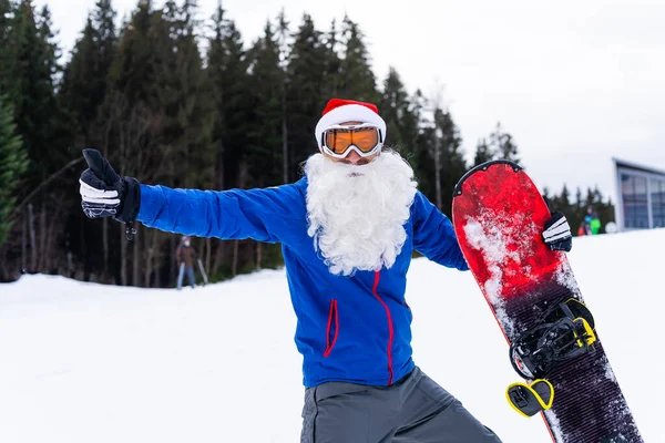 Noel Baba şapkalı bir adam kayak merkezinde snowboard yapıyor.. — Stok fotoğraf