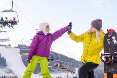Snowboard yapan anne ve kızı karda oynuyorlar.