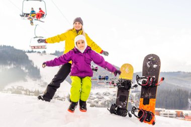 Snowboard yapan anne ve kızı karda oynuyorlar.