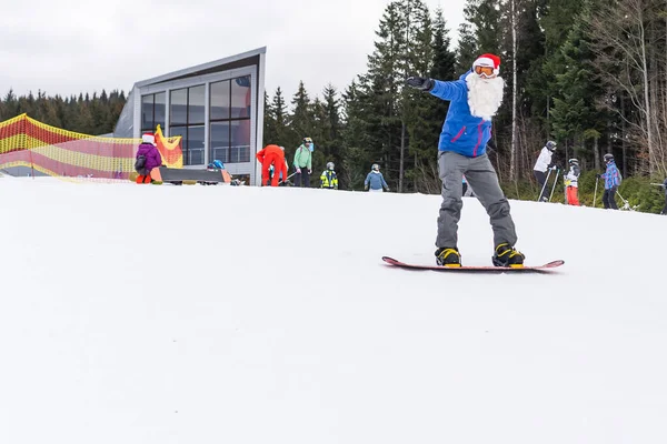 Homem feliz em santa chapéu de Natal vermelho com snowboard no inverno montanhas colina — Fotografia de Stock