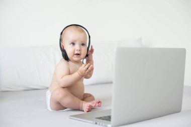 Beyaz yatakta dizüstü bilgisayarı olan şirin bir bebek.