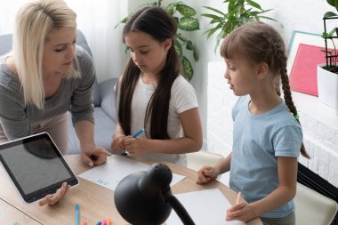 Güzel genç anne, kızlarına ödevlerinde yardım ediyor..