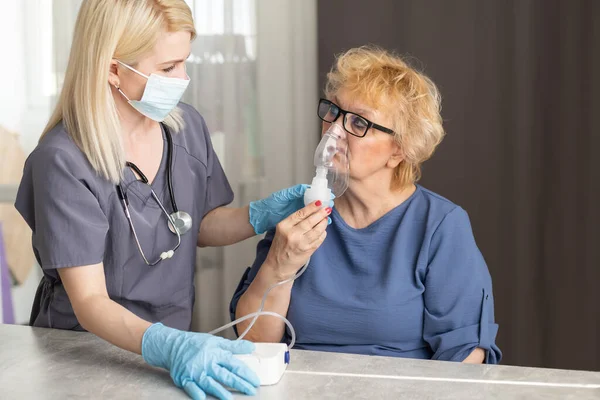 Junge Ärztin hält Sauerstoffmaske über dem Gesicht einer Seniorin. — Stockfoto