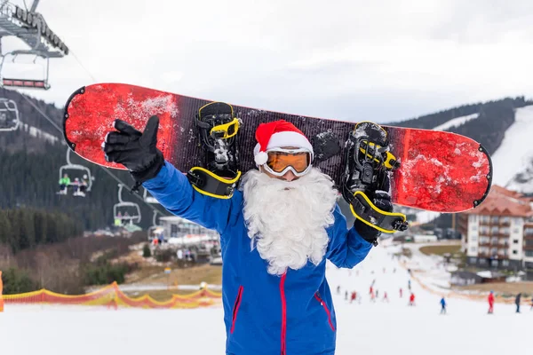 Homem feliz em santa chapéu de Natal vermelho com snowboard no inverno montanhas colina — Fotografia de Stock