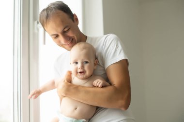 Baba beyaz yatak odasında yeni doğmuş bebeğe sarılıyor..