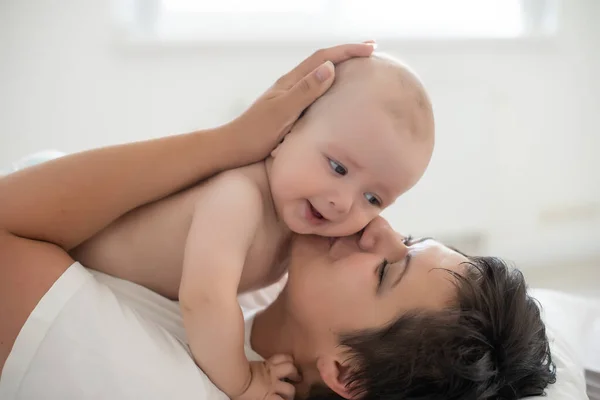 Mutlu bir aile. Anne ve bebek yatakta oynuyor ve gülümsüyor. — Stok fotoğraf