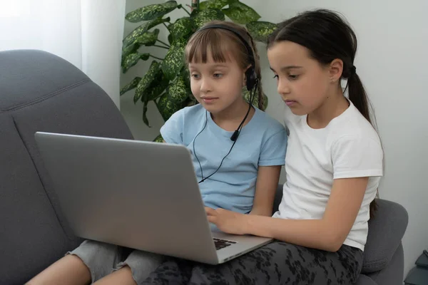 As crianças recebem educação em casa em uma sala de aula com um laptop, cursos on-line para crianças, desenvolvimento infantil, duas meninas caucasianas se divertir e assistir desenhos animados, casa — Fotografia de Stock