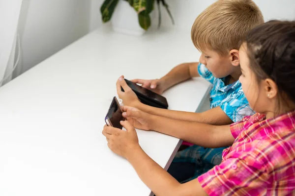 Jongen spelen met smartphone naast zijn zus in de kamer thuis. — Stockfoto