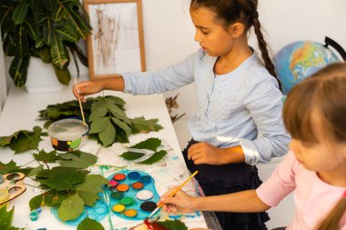İki liseli kız yaprakları boyuyor.