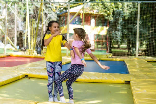 Malé krásné dívky baví venkovní. Skákání na trampolíně v zóně dětí. Zábavní park — Stock fotografie