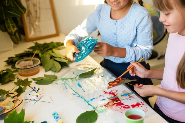 Girls paint patterns autumn leaf. Gouache, brush and various autumn leaves on a wooden table. Childrens art project. Colorful Hand-painted on dry autumn leaves — Stock Photo, Image