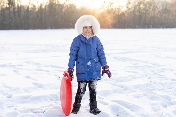 Linda niña en ropa de invierno juega en el parque con trineos. las vacaciones de invierno —  Fotos de Stock