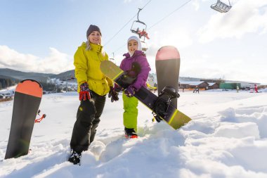 Snowboard yapan anne ve kızı karda oynuyorlar.
