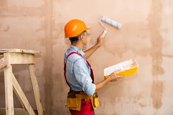 Reparación, construcción, construcción, personas y concepto de mantenimiento - hombre sonriente con casco sobre fondo de pared —  Fotos de Stock