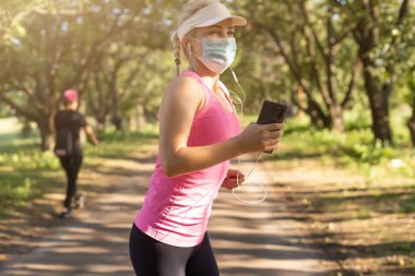 Karantina sırasında formda kalın. Spor yapan genç bir kadın dışarıda koşuyor, yüzünde koruyucu bir maske var. Corona virüsünden ya da Covid-19 'dan tek başına kaçmak.