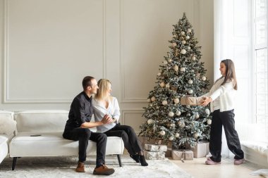Mutlu Noeller ve mutlu tatiller. Anne, baba ve çocuk hediye değiş tokuşu. Ebeveynler ve kızları kapalı alanda eğleniyorlar. Odada hediyeleri olan sevgi dolu bir aile. Yüksek kalite fotoğraf