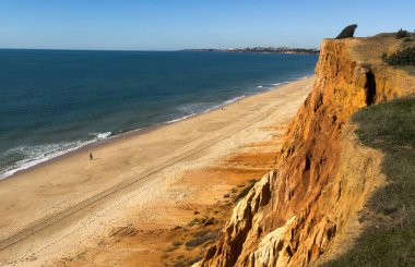 Kızıl kayalıkları ve kayalıkları olan güzel kumlu bir sahil. Günbatımında Portekiz, Praia Algarve 'deki Atlantik kıyısında sığ dalgalarla birlikte. Yüksek kalite fotoğraf