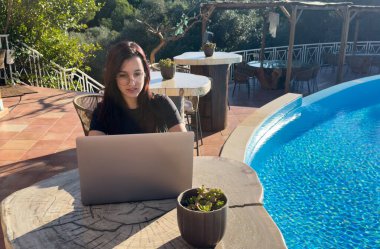 Yaz tatili sırasında havuz kenarında dizüstü bilgisayarda çalışan İspanyol bir kız. Yüksek kalite fotoğraf