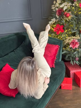 Güzel genç bir kadın Noel günü evde dinleniyor, Noel ağacının yanında kanepede oturuyor. Yüksek kalite fotoğraf