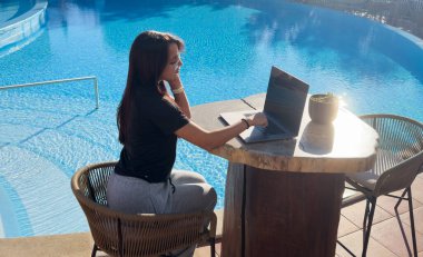 Havuz başında dizüstü bilgisayar kullanan bir kız, modern teknolojiyle rahat bir atmosfer, rahat bir çalışma alanı ve boş zaman konsepti. Yüksek kalite fotoğraf