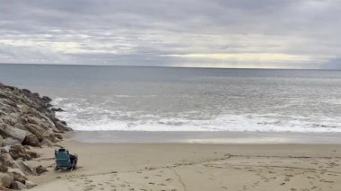 Gün batımında geniş beyaz bir kumsal, bulutlu bir gökyüzünün altında hafif dalgalar akıyor. İnsanlar kıyıda, deniz kenarındaki huzurlu ve sessiz atmosferin tadını çıkarıyorlar. Portekiz. Yüksek kalite fotoğraf