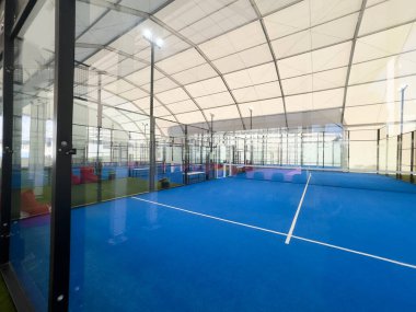 Metal çitler ve tepedeki parlak ışıklarla çevrili canlı mavi bir yüzeye sahip geniş bir kapalı saha, iyi korunmuş bir spor tesisi içinde antrenman veya rekabetçi maçlar için mükemmel. Yüksek kalite fotoğraf