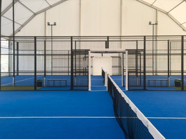 Metal çitler ve tepedeki parlak ışıklarla çevrili canlı mavi bir yüzeye sahip geniş bir kapalı saha, iyi korunmuş bir spor tesisi içinde antrenman veya rekabetçi maçlar için mükemmel. Yüksek kalite fotoğraf