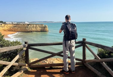 Gezgin, seyahat fotoğraflı sırt çantasıyla uçurumların harika fotoğraflarını çekiyor. Gezgin fotoğrafçı, fotoğraf makinesinin görüş açısıyla deniz manzarası çekiyor. panoramik seyahat fotoğrafçılığı. Yüksek kalite fotoğraf